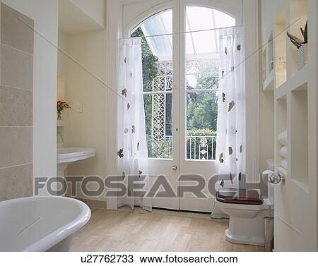 Patterned white voile curtains on French doors in modern white bathroom with wooden flooring View Large Photo Image Stock Image - Patterned white voile curtains on French doors in modern white bathroom with wooden flooring. Fotosearch