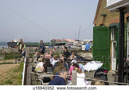 Stock Image - People sitting at tables outside restaurant on the beach at Whitstable in Kent. Fotosearch