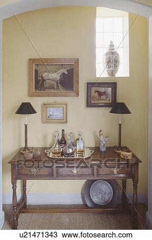 Stock Image - Pictures above lamps and drinks tray on antique table in diningroom alcove. Fotosearch