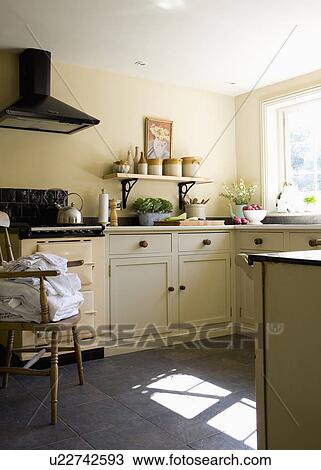 Stock Image - Pile of sheets on chair beside cream Aga in country kitchen. Fotosearch