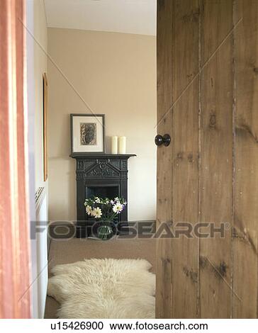 Stock Image - Pine door open to small cottage bedroom with sheepskin rug on the floor. Fotosearch