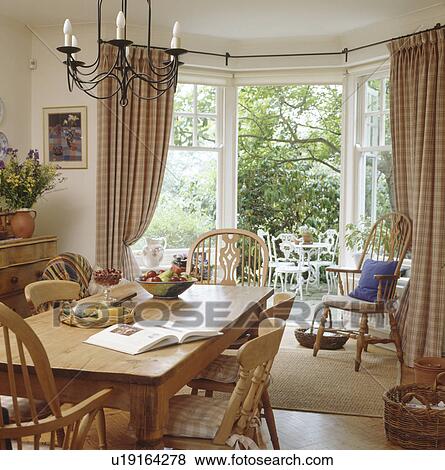 Pine table and chairs in neutral diningroom with checked curtains on open French doors with vie of the garden View Large Photo Image Stock Photo - Pine table and chairs in neutral diningroom with checked curtains on open French doors with vie of the garden. Fotosearch