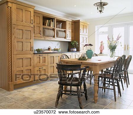Pine table and Windsor chairs in country kitchen with fitted oak cupboards and units and ceramic floor tiles View Large Photo Image Stock Image - Pine table and Windsor chairs in country kitchen with fitted oak cupboards and units and ceramic floor tiles. Fotosearch