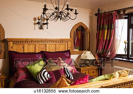 Pink and red cushions piled on bed with wooden headboard in bedroom with black metal light fitting View Large Photo Image Stock Photography - Pink and red cushions piled on bed with wooden headboard in bedroom with black metal light fitting. Fotosearch