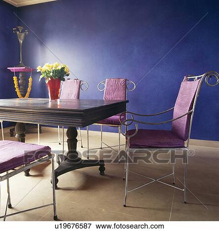 Stock Photo - Pink cushions on metal chairs at wood table in blue dining room with limestone flooring. Fotosearch