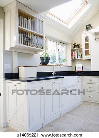Stock Image - Plate rack above fitted unit with black granite worktop in modern white kitchen extension. Fotosearch