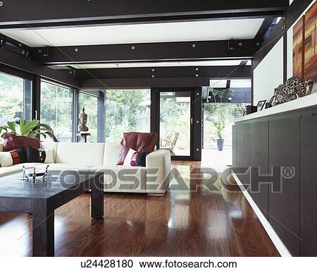 Stock Image - Polished wooden flooring in large modern living room with white sofa and black ceiling beams. Fotosearch