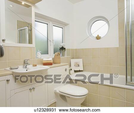 Porthole Window Above Bath In Modern Bathroom With Neutral Tiles
