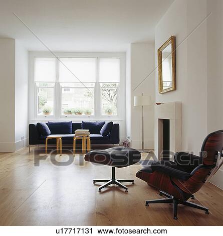 Stock Image - Reclining chair and stool beside fireplace in modern white living room with wooden flooring. Fotosearch