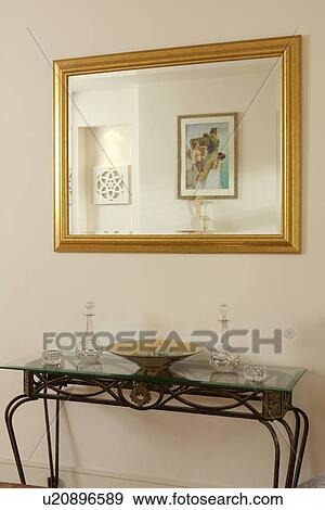 Stock Photo - Rectangular gilt mirror above metal console table. Fotosearch