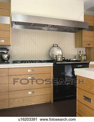 Stock Image - Rectangular stainless steel extractor above black Aga oven in modern kitchen. Fotosearch
