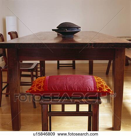 Stock Photo - Red silk cushion on stool at wooden table in modern dining room. Fotosearch