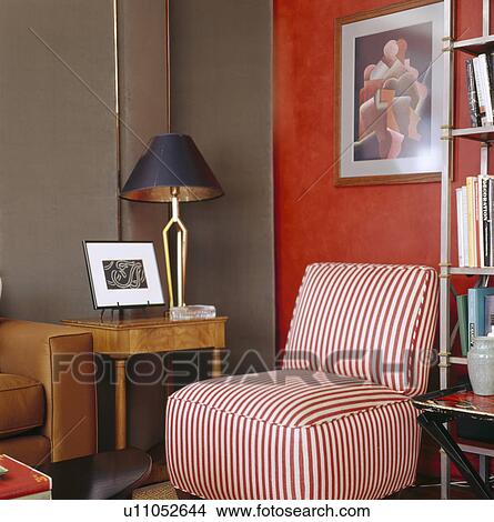 Picture - Red & white striped upholstered chair beside small table with black lamp in corner of red and beige living room. Fotosearch