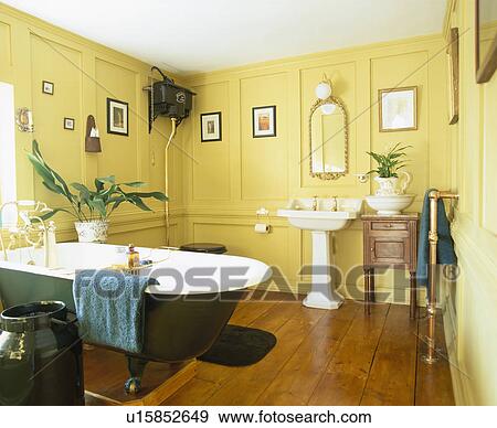 Stock Photo - Roll-top bath and white pedestal basin in yellow panelled bathroom with wooden flooring. Fotosearch