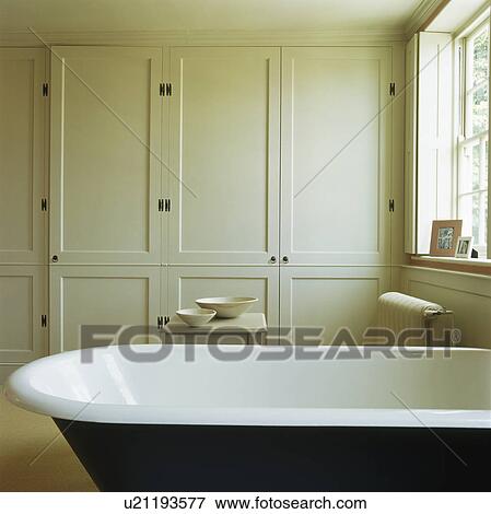 Stock Photo - Rolltop bath in contemporary townhouse bathroom with fitted storage cupboards. Fotosearch