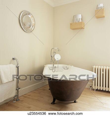 Stock Photograph - Rolltop bath in corner of cream bathroom with wooden flooring. Fotosearch