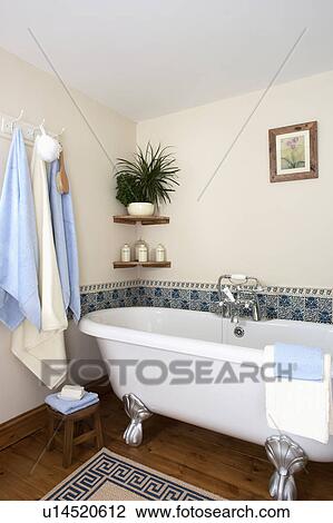 Stock Image - Rolltop bath in cream bathroom with tiled border. Fotosearch
