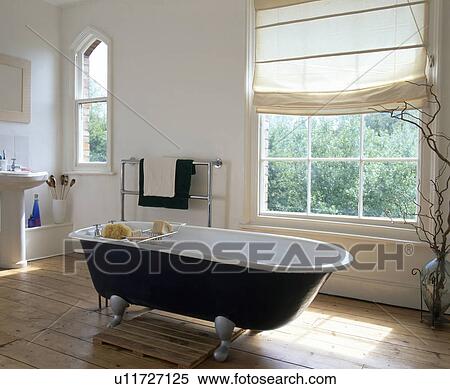 Stock Photography - Rolltop bath in front of window with white blind in white bathroom with wooden flooring. Fotosearch