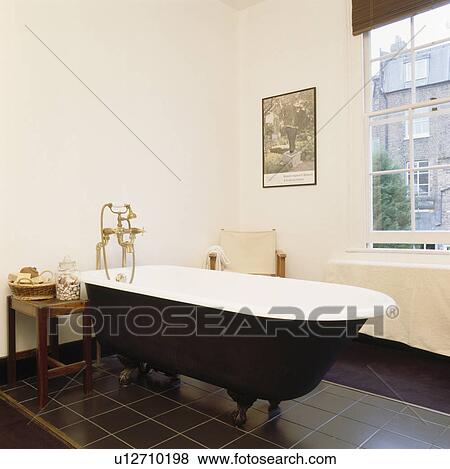 Stock Photo - Rolltop bath in modern white bathroom with black tiled floor. Fotosearch