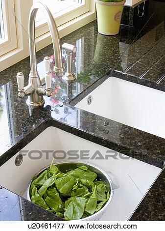 Stock Photo - Salad greens in colander in underset double white sink below chrome mixer tap in modern kitchen. Fotosearch