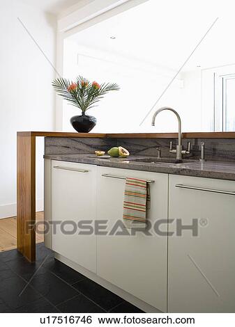 Stock Photograph - Sink and chrome mixer-tap in fitted unit with black granite worktop and white melamine cupboard doors. Fotosearch