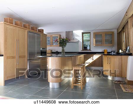 Stock Photo - Slate flooring and island unit in modern kitchen with fitted wood units. Fotosearch