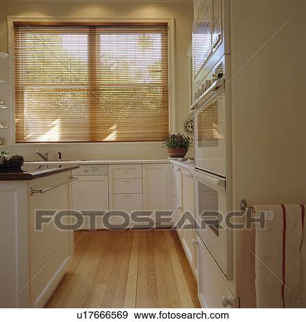 Stock Photo - Slatted wooden blind and wooden flooring in modern white kitchen. Fotosearch