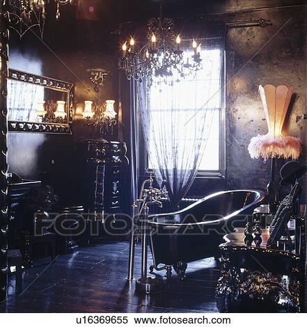 Stock Photography - Slipper bath in opulent black bathroom with chandelier and wall lights and feather trimmed lampshade. Fotosearch