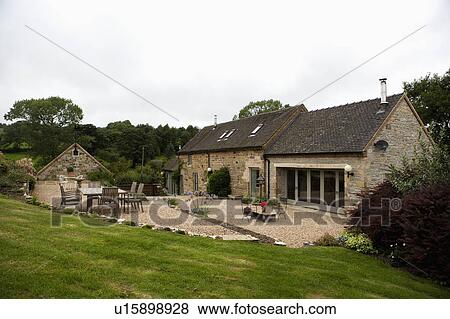 Stock Photo - Sloping lawn down to traditional stone barn conversion with gravel terrace. Fotosearch
