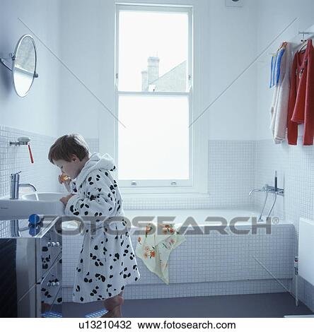 Stock Image - Small boy cleaning his teeth in modern white bathroom. Fotosearch
