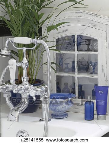 Stock Photography - Small white cupboard with collection of blue china on side of bath with chrome showerhead and taps. Fotosearch