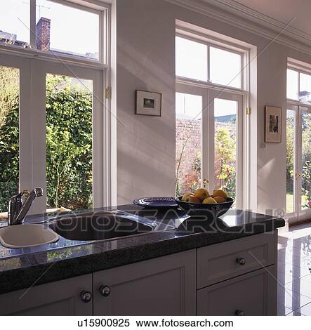 Stock Photography - Stainless steel and white ceramic sinks in black granite topped unit in front of window. Fotosearch