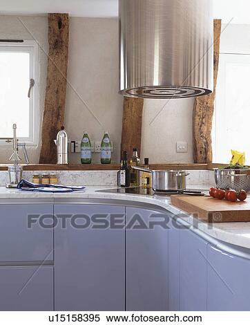 Stock Photography - Stainless steel cylindrical extractor above corner hob in modern kitchen with pale blue fitted units. Fotosearch