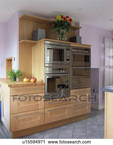 Stock Image - Stainless steel double ovens in pale wood unit in modern mauve kitchen. Fotosearch