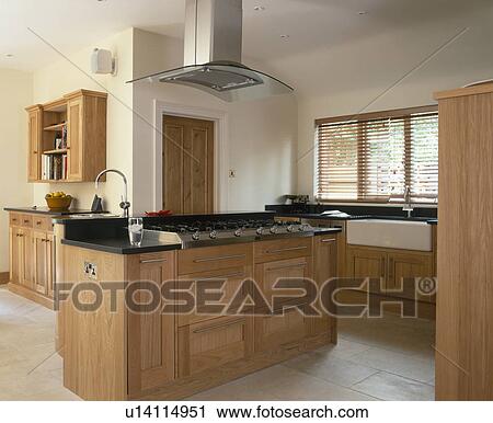 Stock Image - Stainless steel extractor above pale wood fitted island unit in modern kitchen. Fotosearch