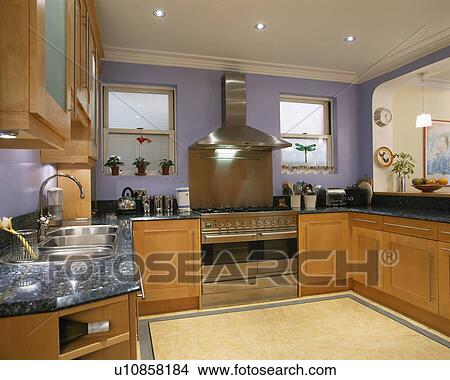 Picture - Stainless steel extractor and range oven in modern blue kitchen with fitted wood units. Fotosearch