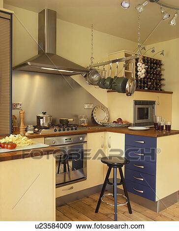 Stock Photo - Stainless steel extractor and splashback above steel oven in modern cream kitchen with pans on steel storage rack. Fotosearch