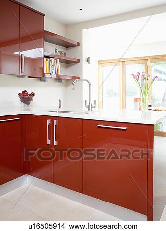 Stainless steel mixer tap and underset sink in red fitted peninsular unit with white worktop in modern kitchen View Large Photo Image Picture - Stainless steel mixer tap and underset sink in red fitted peninsular unit with white worktop in modern kitchen. Fotosearch