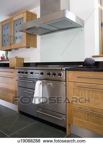 Stock Photo - Stainless-steel range oven and extractor hood in modern kitchen with fitted wood units. Fotosearch