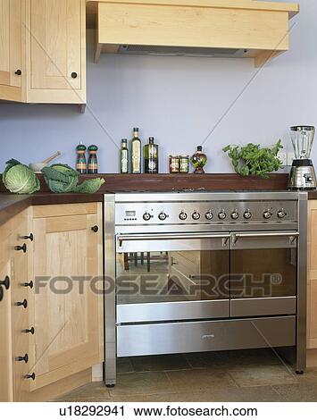 Stock Image - Stainless steel range oven in modern kitchen with pale wood units. Fotosearch