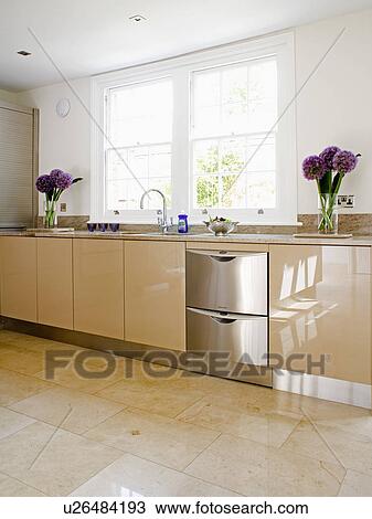 Stock Image - Stainless-steel wine cooler in shiny cream fitted unit in modern white kitchen. Fotosearch