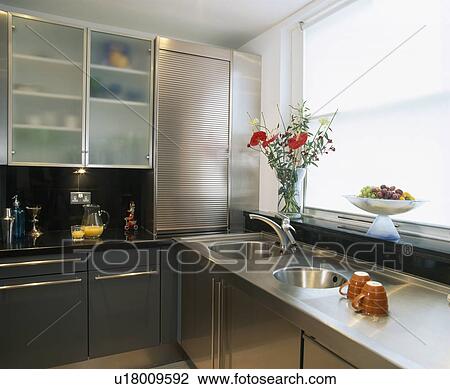 Stock Image - Stainless steel worktop and units in modern kitchen with glazed doors on fitted unit. Fotosearch