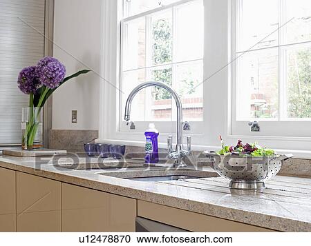 Stock Image - Steel colander on worktop beside chrome mixer tap and underset stainless-steel double sinks . Fotosearch