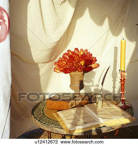 Stock Image - Still-Life of exotic red flowers in stone urn on small circular table with old books. Fotosearch
