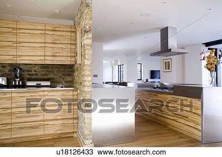 Stock Image - Stone-clad dividing wall in modern white kitchen extension with pale wood and stainless steel fitted units. Fotosearch
