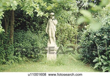 Stock Photo - Stone statue on plinth in front of hedge in country garden. Fotosearch