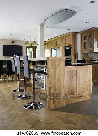 Stock Photography - Stools at breakfast bar in modern kitchen with parquet flooring and pale wood fitted units. Fotosearch
