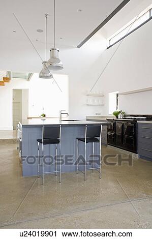 Stools at breakfast bar on grey island unit in modern white ktichen with concrete flooring View Large Photo Image Stock Image - Stools at breakfast bar on grey island unit in modern white ktichen with concrete flooring. Fotosearch