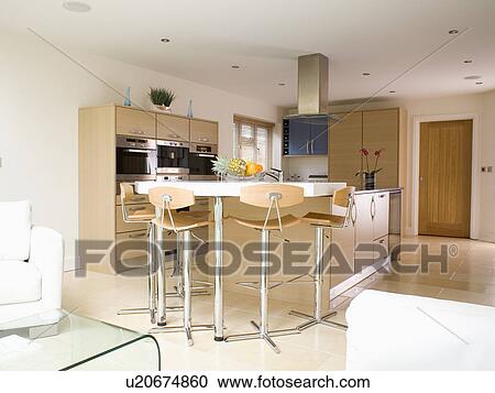 Stock Image - Stools at breakfast bar on island unit in large modern kitchen. Fotosearch