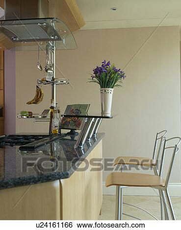 Stock Photograph - Stools at breakfast bar on island unit with granite worktop and stainless steel shelves. Fotosearch